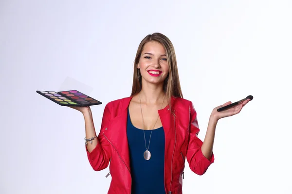 Joven hermosa mujer sostiene en una mano y una paleta con pintura y sombras para el maquillaje, cepillo de segunda mano para maquillaje — Foto de Stock