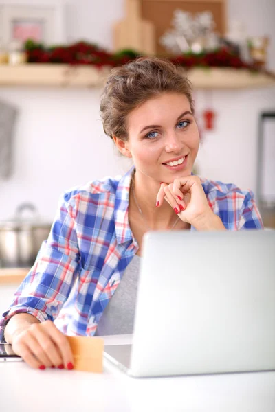 Mulher sorrindo compras on-line usando computador e cartão de crédito na cozinha — Fotografia de Stock