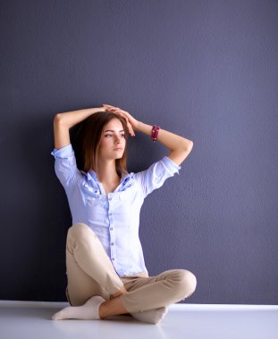 Genç bir kadın yerde, kara duvarın yanında oturuyor.