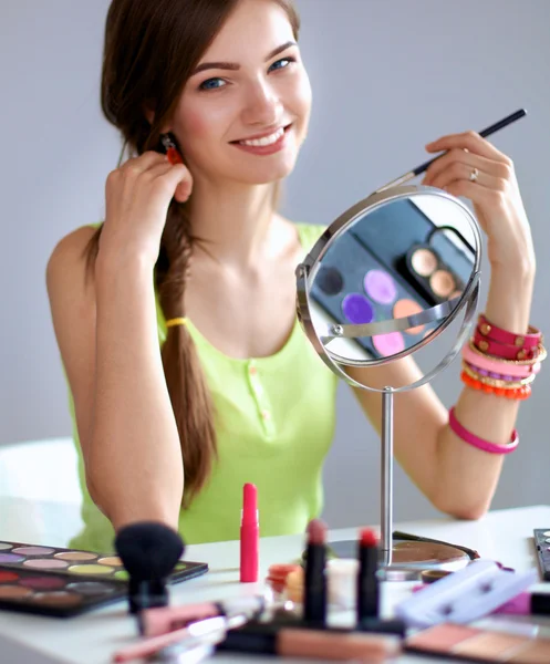 Joven hermosa mujer haciendo maquillaje cerca del espejo, sentado en el escritorio — Foto de Stock