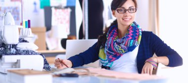 Güzel moda tasarımcısı stüdyoda masada oturuyor.