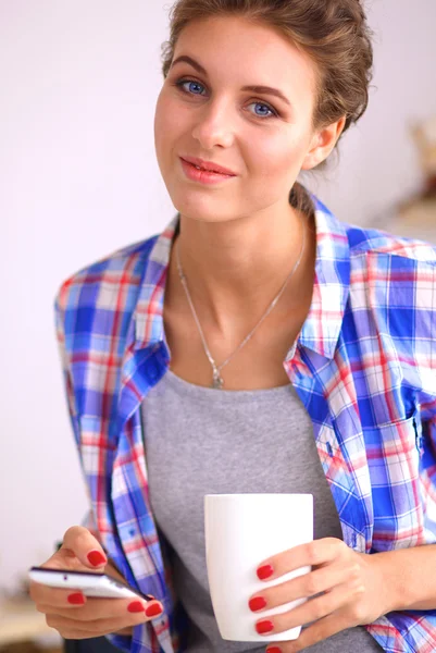 Sorrindo mulher segurando seu celular na cozinha — Fotografia de Stock