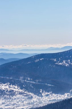 Göz kamaştırıcı kış dağ manzarası. Orman ve karla kaplı dağlar, dağların tepelerinde sarkan tüylü bulutlar 