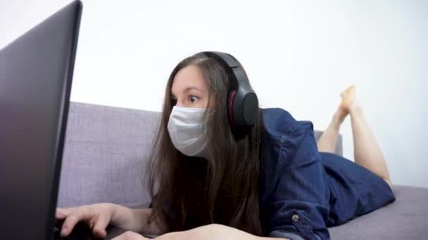 Ένα κορίτσι με μια ιατρική μάσκα στο πρόσωπό της σε ένα φορητό υπολογιστή. — Αρχείο Βίντεο