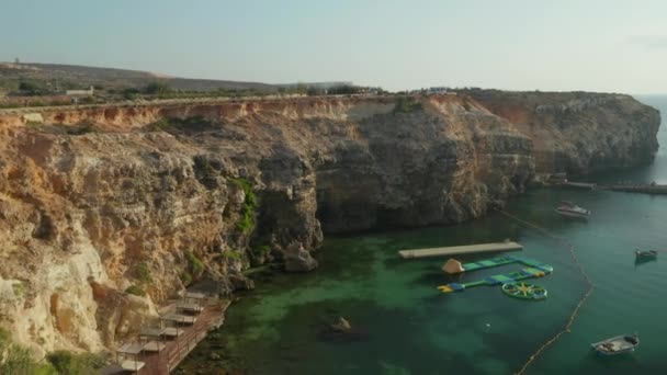 马耳他戈佐岛Popeye村的热带锚地湾，有水上平台，日落时没有人与绿松石水，空中景观 — 图库视频影像