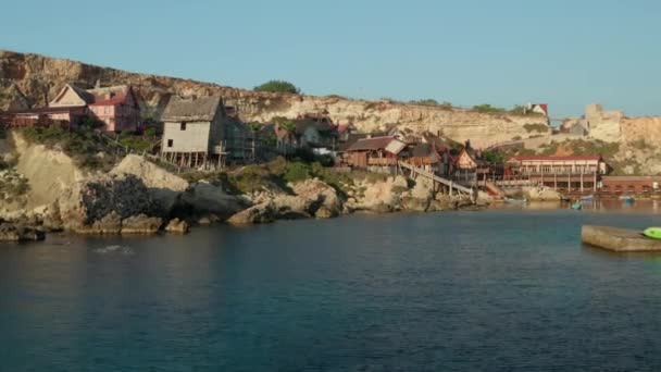 Aerial Establishing Shot of Popeye Village en Anchor Bay, Gozo Island, Malta Casas de pueblo de madera por el agua, Aerial Drone Shot forward Dolly — Vídeos de Stock