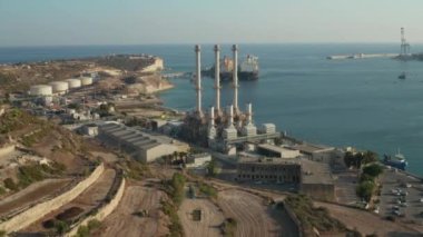 Akdeniz adası Malta 'da su kenarında üç büyük bacası olan bir fabrika.