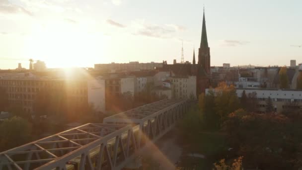 Желтый поезд метро, проезжающий через Берлин, Германия, мимо Красной церкви в красивом свете заката, воздушный дрон с видом на Англ — стоковое видео