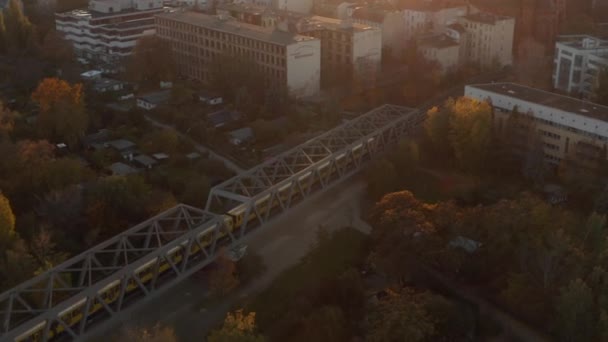 Tracking groothoek Shot of Yellow Subway trein passeert brug door Berlijn, Duitsland in de herfst Zonsondergang licht, antenne perspectief — Stockvideo