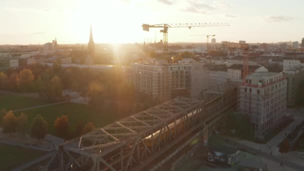 Gele trein op brug boven Openbaar park met mensen die van hun zonsondergang genieten in Berlijn, Duitsland, Uitzicht vanuit de lucht — Stockvideo