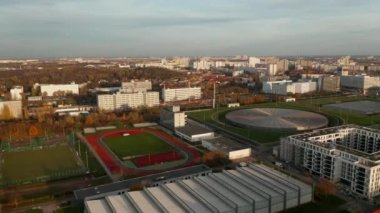 Berlin, Almanya 'da Yenilikçi Velodrome Binası Bisiklet Arenası ile Kentsel Şehir Bölgesi' nde Kırmızı Koşu Pisti Spor Sahası, Sunset 'te solda Hava Kaydırma Dümeni