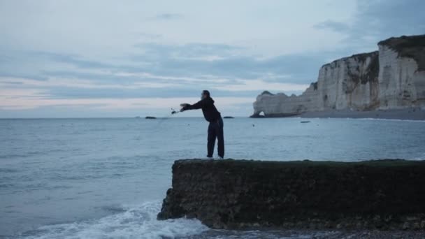Man fishing with Mask on by Etretat cliffs in France with ruff Ocean waves crashing on rocks — Stock Video