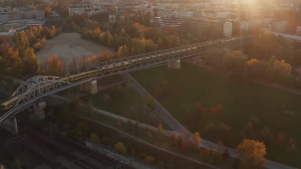 2 trenes amarillos del metro que pasan por el puente sobre el parque público con árboles de color rojo y naranja de otoño en la luz del atardecer, gran angular aéreo que establece tiro — Vídeos de Stock