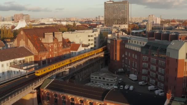 Typisch Berlijn Gele metro Trein op hoge grond die door de buurt van de stad in prachtige gouden uur Zonsondergang licht, Luchtfoto volgen volgen groothoek — Stockvideo