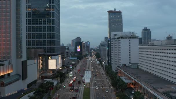 Tiro aéreo de dolly volador bajo del tráfico ocupado de la ciudad en el centro moderno de la ciudad en el atardecer en Yakarta, Indonesia — Vídeo de stock