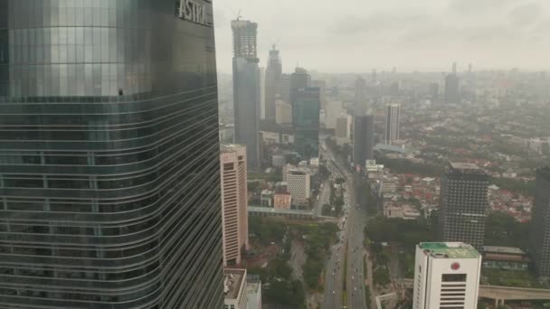 Vista aérea revelan volar desde detrás de un rascacielos a amplia vista del horizonte de la ciudad de Yakarta revelan en tiempo nublado — Vídeos de Stock