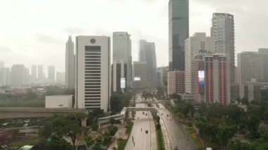 Jakarta, Endonezya 'da yağışlı bir günde, uzun gökdelenlerle şehre giden çok şeritli bir otoyoldaki trafiği takip eden hava kulesi görüntüsü