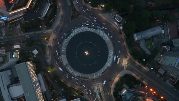 Ptaki lotnicze Oko nad głową Obrót w dół Widok ruchliwego ruchu miejskiego na rondzie pomnika Selamat Datang nocą — Wideo stockowe