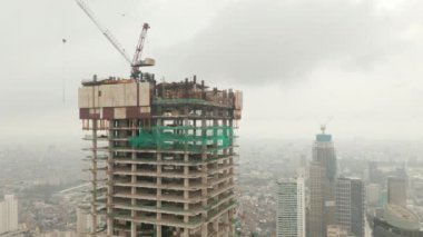 Bulutlu bir günde şehir merkezinde yapım aşamasındaki yüksek gökdelenin havadan eğimli kaidesel görüntüsü