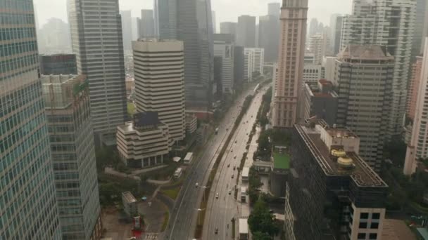 Aumento del disparo aéreo que se inclina hacia la vista aérea del tráfico de automóviles en una carretera de varios carriles rodeada de rascacielos altos en Yakarta, Indonesia — Vídeo de stock