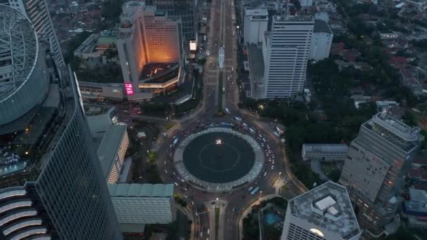 Inclinação aérea horizontal à vista aérea de um tráfego movimentado em uma rotunda do Monumento Selamat Datang cercada por arranha-céus modernos em Jacarta, Indonésia — Vídeo de Stock