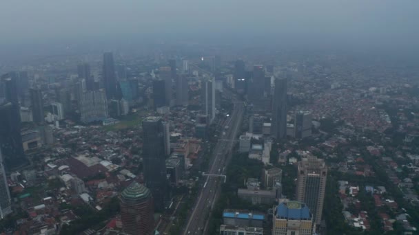 Aerea ampio colpo lento di autostrada multi corsia che passa attraverso occupato centro città moderno con grattacieli e densi quartieri residenziali a Jakarta — Video Stock
