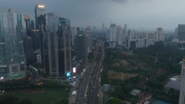 Flygfoto dolly utsikt efter trafik på en upptagen motorväg på kvällen omgiven av höga skyskrapor och idrottsplats i Jakarta — Stockvideo