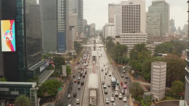 Aerial dolly ritirarsi colpo basso volante di veicoli su una trafficata autostrada a più corsie con auto della polizia e dei trasporti pubblici nel moderno centro della città di Jakarta — Video Stock