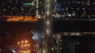 Gece şehir merkezindeki çok şeritli yolda sokak ışıklarıyla aydınlatılan araba trafiğini yukarıdan gören tepeden aşağı uçan kuşlar.
