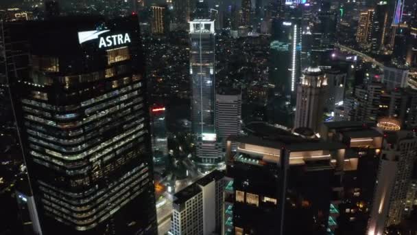 Primer plano volar por tiro aéreo de rascacielos altos modernos por la noche con tráfico de coches ocupados por debajo en Yakarta — Vídeo de stock