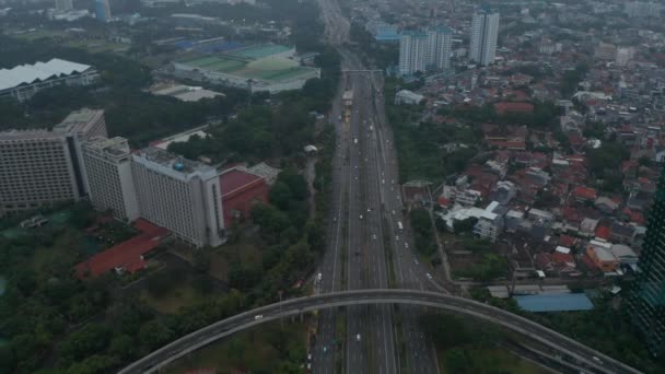 Tiro de inclinación de dolly aérea después de coches en una carretera de varios carriles y revelando una amplia vista del horizonte urbano moderno de la ciudad de Yakarta, Indonesia — Vídeo de stock