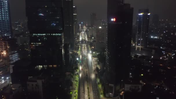 雅加达市中心一座高耸的摩天大楼环绕着一条空荡荡的多车道公路，一辆警车在夜间驶过一条空旷的多车道公路时被空中拍到 — 图库视频影像