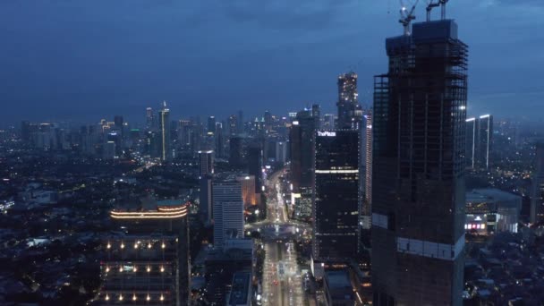 Vue aérienne du paysage urbain de Jakarta la nuit avec de grands gratte-ciel et un trafic achalandé autour du rond-point du monument Selamat Datang — Video