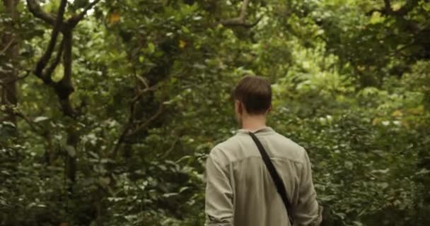 Junger kaukasischer Mann im khakifarbenen Hemd spaziert allein durch den tropischen Regenwald von Bali — Stockvideo