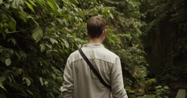 Costas boneca tiro de um jovem homem branco caminhando através de uma floresta tropical com vegetação exuberante em Bali. — Vídeo de Stock