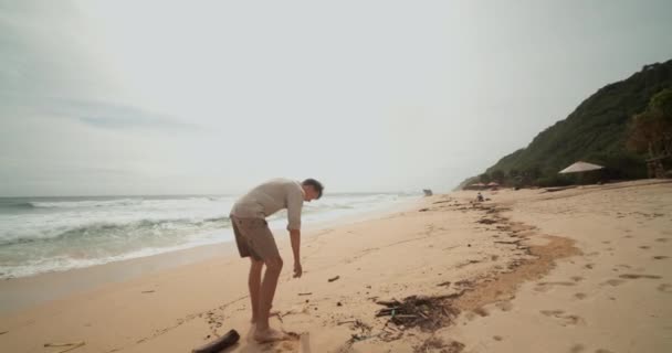 Close up vista circundante de jovem do sexo masculino pegar o lixo em uma praia tropical arenosa em Bali. Homem limpando a praia durante as férias — Vídeo de Stock
