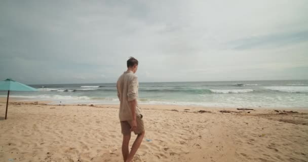 Jovem caucasiano macho caminhando na praia em Bali em shorts cáqui e camisa — Vídeo de Stock