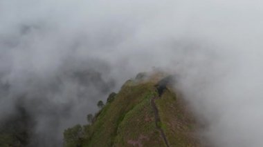 Sis ile çevrili aktif bir volkanın tepesindeki dağların tepesindeki kırık bir yüzeyin havadan görüntüsünü kapatın.