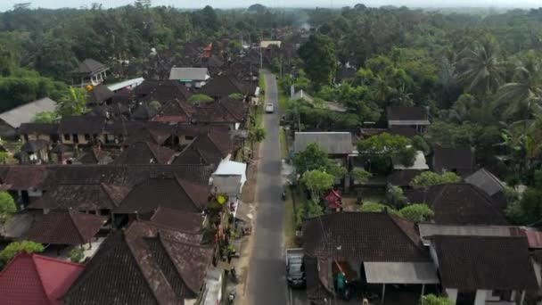 Aerial tilting dolly shot following the truck driving on the road through traditional residential neighborhood in small town in Bali, Indonesia — Wideo stockowe