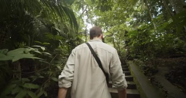 После фотографии молодого человека, поднимающегося по лестнице к каменным столбам древних руин в тропических лесах Бали. — стоковое видео