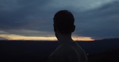 Dağın zirvesinde, Endonezya 'nın Bali kentindeki Batur Dağı' nda güneşin doğuşuna ya da batışına doğru çevreye bakan beyaz erkeğin arkasını yakından görürüz.