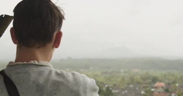 Close-up tiro de um homem em um ponto de vista apontando para a paisagem panorâmica no vale chuvoso abaixo em Bali, Indonésia — Vídeo de Stock