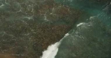 Suyun üzerinde hareket eden sığ bir dalganın yavaş çekim görüntüsünü kapatın ve kayalık tropikal plaj Emerald yeşil ve mavi okyanus sularını dalgalarla vurun.