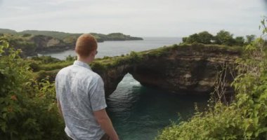 Endonezya, Bali 'de, Nusa Penida' daki kırık plaja bakan uçurumda kızıl saçlı bir adamın yakın görüntüsü.