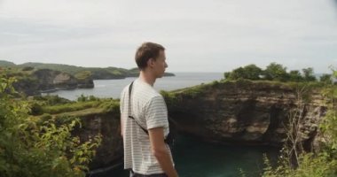 Endonezya 'nın Bali kentinde, Nusa Penida' da kırılan plajın yukarısındaki kayalıklarda çantalı bir erkek turisti çevreleyen yakın çekim.