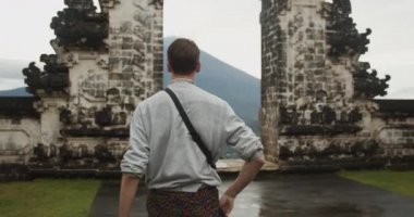 Pura Penataran Agung Lempuyang tapınağında ve Bali 'deki Agung Dağı yanardağında Cennetin Kapıları' na doğru yürüyen beyaz bir erkek turistin orta ölçekli görüntüsünü kapatın.