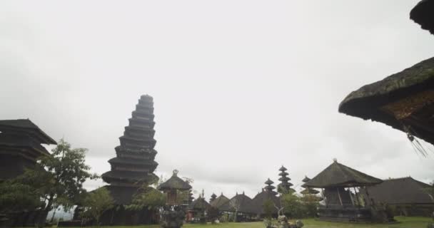 Tiltning dolly skott av gräsbevuxen tempel grunder med svart sten statyer, höga pagoder och religiösa byggnader i Besakih Temple i Bali, Indonesien — Stockvideo