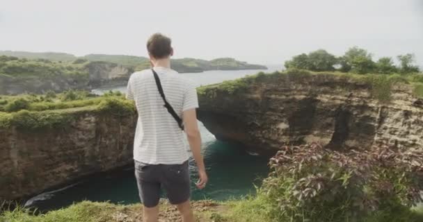 Close up médio tiro de um turista masculino em Bali olhando para arcos deslumbrantes e falésias de Broken Beach Pasih Uug Man de pé no penhasco com vista para o oceano — Vídeo de Stock