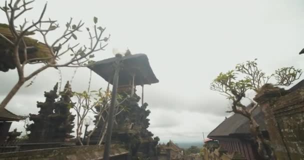 Dolly girato inclinando verso il basso di camminare per le strette strade circondate da splendide sculture in pietra nera ed edifici religiosi nel tempio di Besakih a Bali, Indonesia — Video Stock