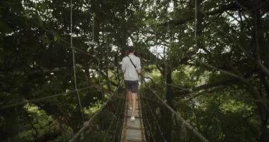 Dolly, Bali 'deki tropikal bir yağmur ormanının üzerindeki ip asılı köprüde dikkatle yürüyen genç bir adamı takip ederken çekildi.